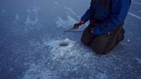 man with fishing rod catches fish in ice hole at frozen lake in trondheim, norway