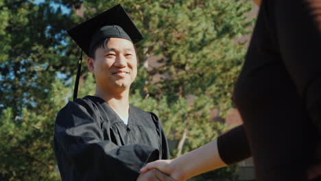 successful asian man in graduate clothes accepts congratulations they shake his hand