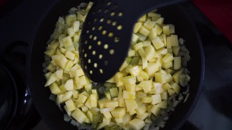 stirring the onion and potatoes in a frying pan