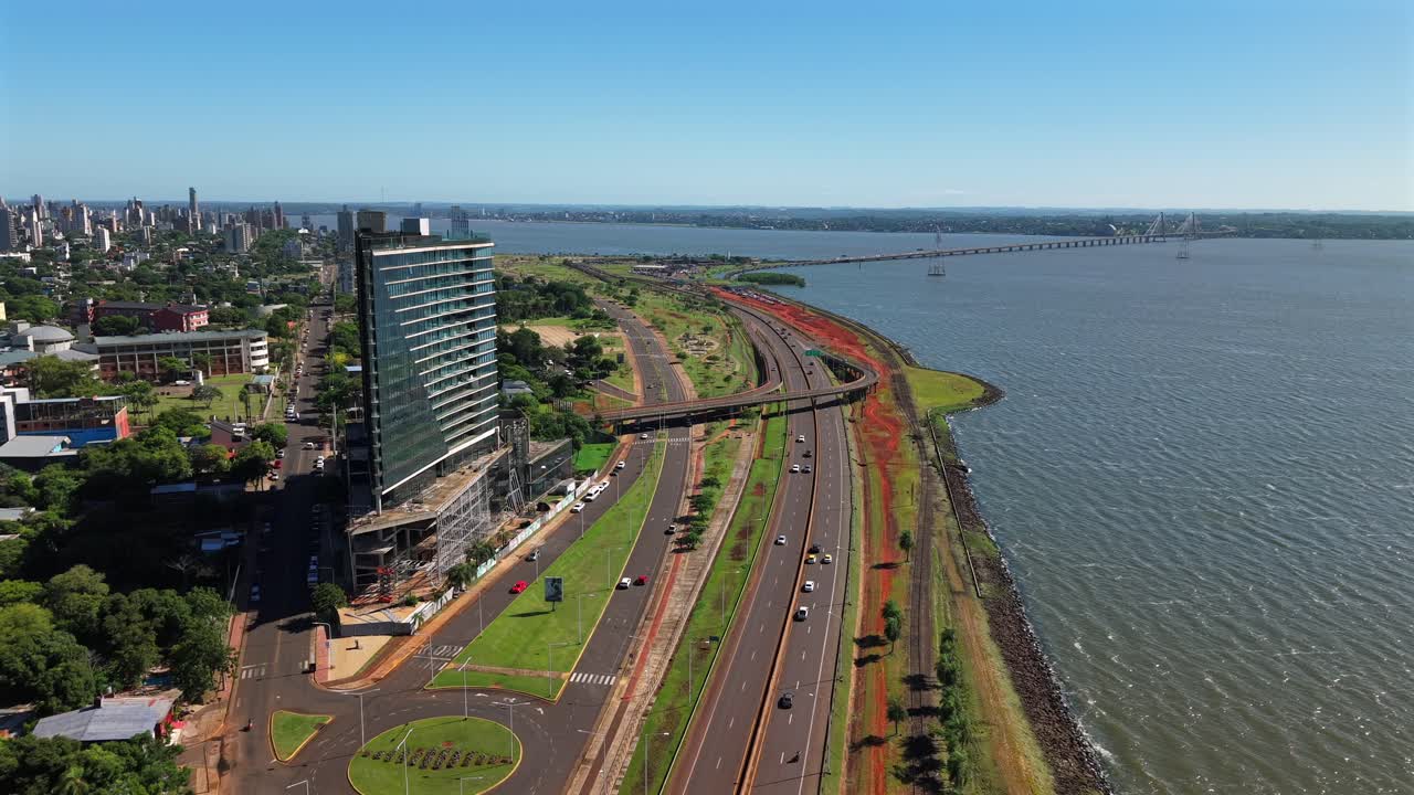 Rekaman drone sudut lebar yang menampilkan menara kaca modern, jalan raya pesisir, dan jembatan menuju Paraguay di Posadas