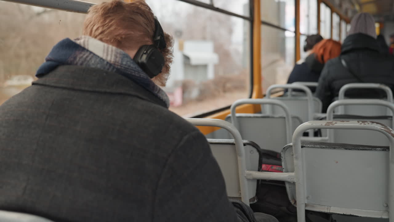 Passeggero che osserva attentamente la vita cittadina. Uomo con le cuffie osserva la scena stradale dal sedile dell'autobus. Individuo contemplativo su un autobus pubblico osserva attentamente le persone e l'ambiente circostante.