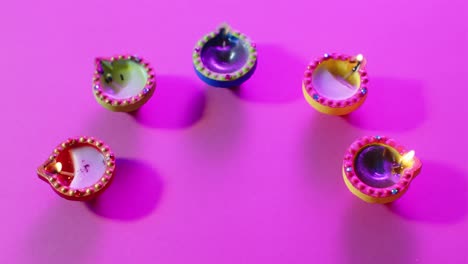 Close-up-of-burning-colourful-candles-celebrating-diwali-on-purple-background