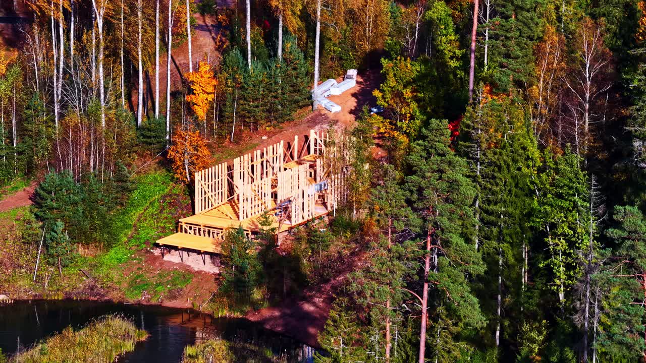 Aerial of new build construction home framing above river winding through autumn forest with red and orange tree canopy