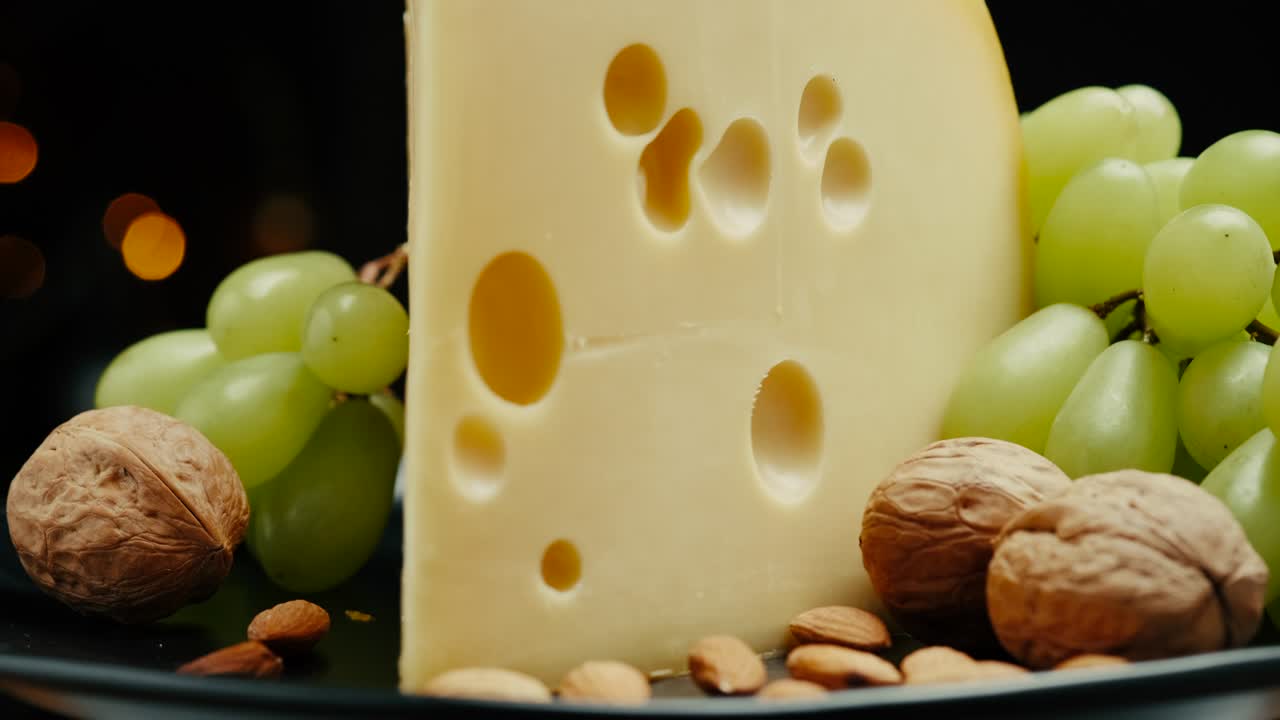 parte cerrada de la cabeza de queso duro medio edam gouda parmesán en tabla de madera, con nueces y uvas girando en el plato