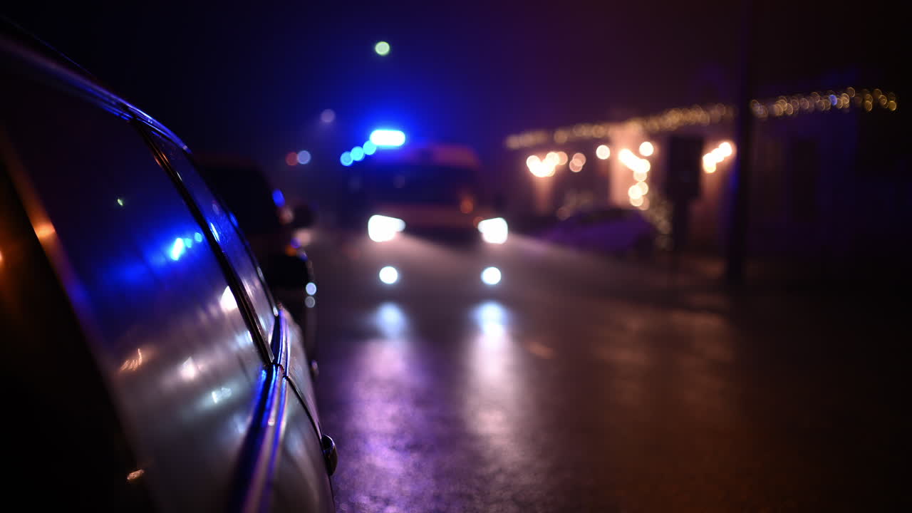 Einsatzfahrzeug nähert sich nachts auf einer nassen Stadtstraße mit blinkenden Blaulichtern