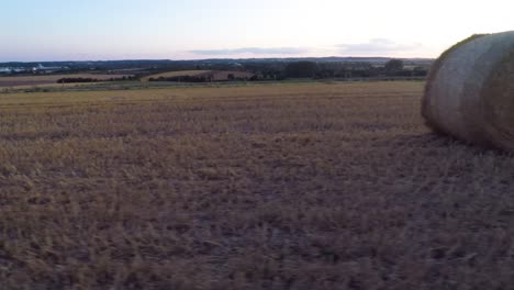 Panning-low-to-the-ground-from-left-to-right-across-a-harvested-field-to-reveal-hay-bales