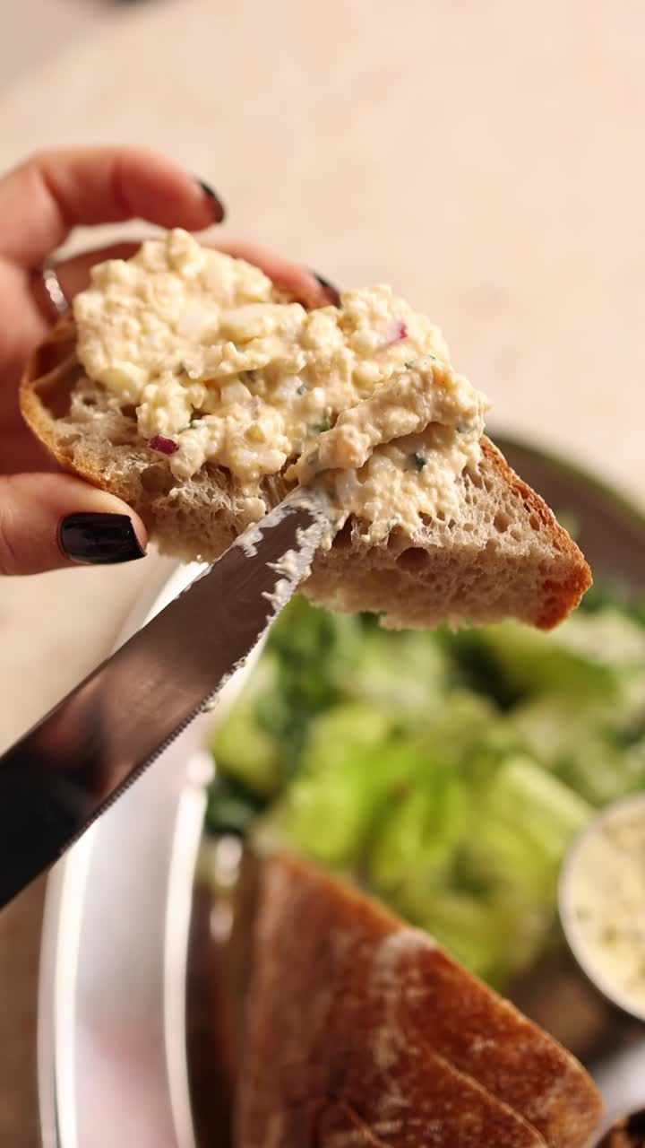 Primo piano di una mano che spalma l'insalata di uova su una fetta di pane