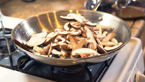 woman's hand adds raw sliced white mushrooms into hot oil in frying pan