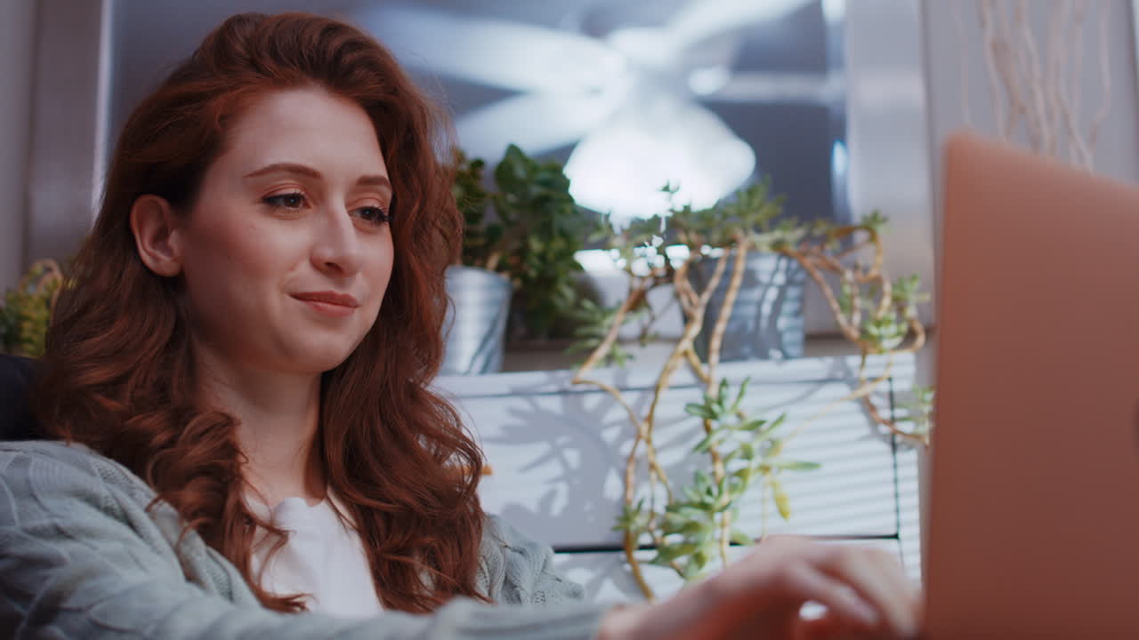 молодая белая женщина работает из дома на своем ноутбуке - приятные нейтральные выражения