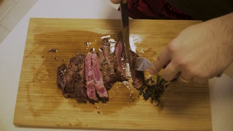 medium rare a4 wagyu steak being cut on wooden chopping board with thyme on the side