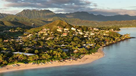 drone aerial view of lanikai beach at sunrise with first morning light hitting mountains behind beachfront real estate on oahu hawaii paradise