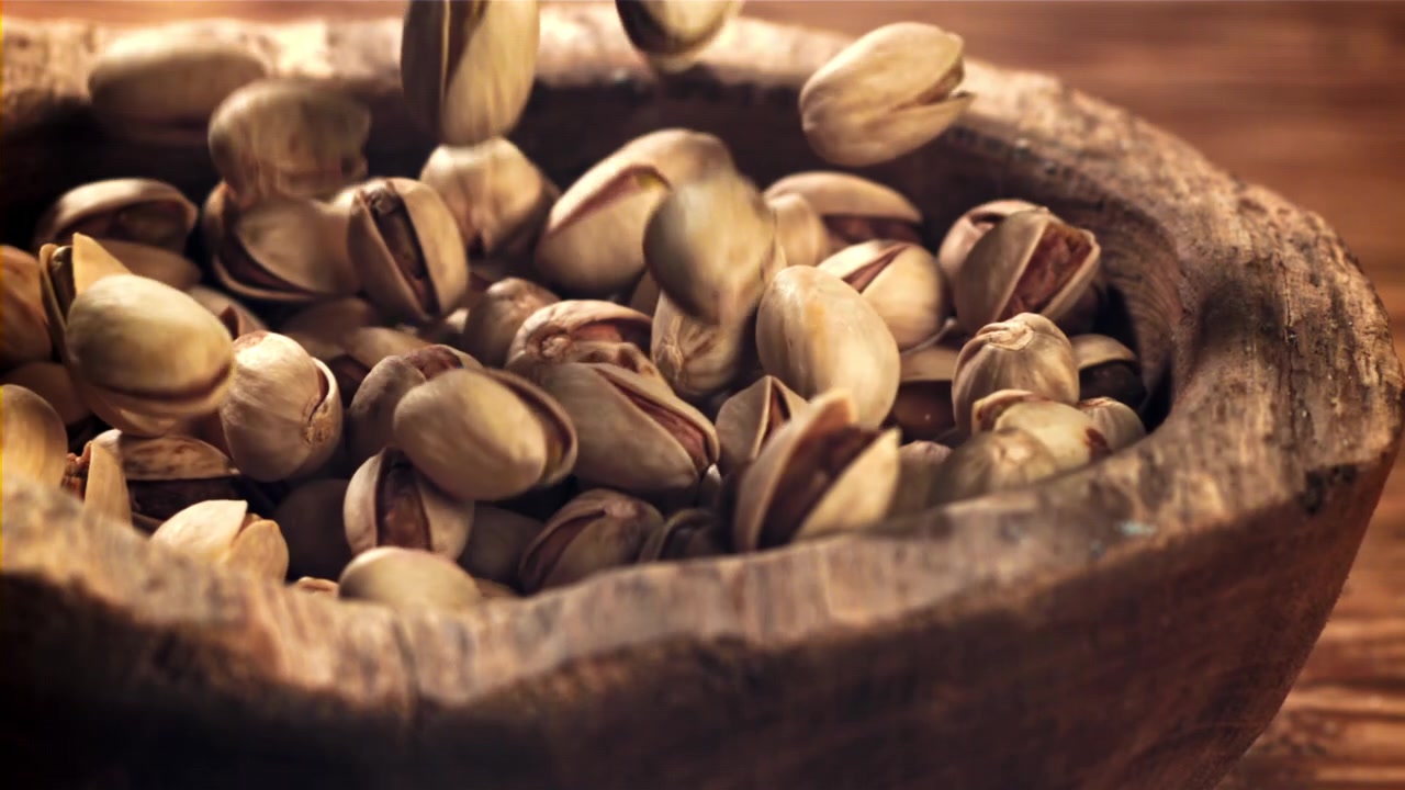 Pistachio Nuts Falling into a Rustic Wooden Bowl in Slow Motion