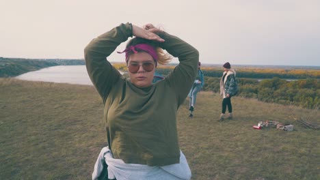 overweight girl fixes hair by friends at camp on green bank