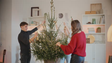 hombre y mujeres decorando el árbol de navidad con luces