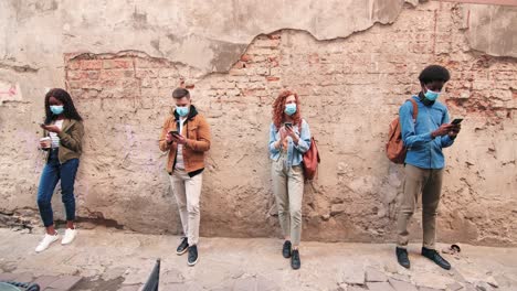 african american and caucasian men and women wearing masks and using smartphone in the street