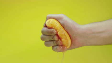 man squeezing an orange to make fresh orange juice cocktail, isolated on a yellow background, slow motion footage