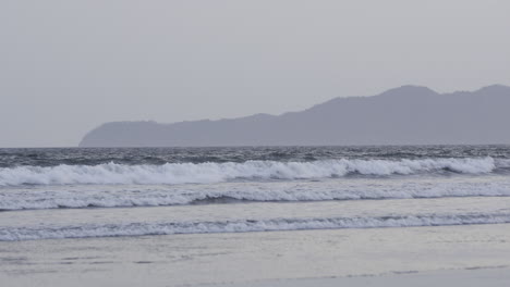 Toma-Estática-De-Olas-Rodando-Hacia-La-Bahía-En-La-Isla-De-Canas-Con-Colinas-Detrás.