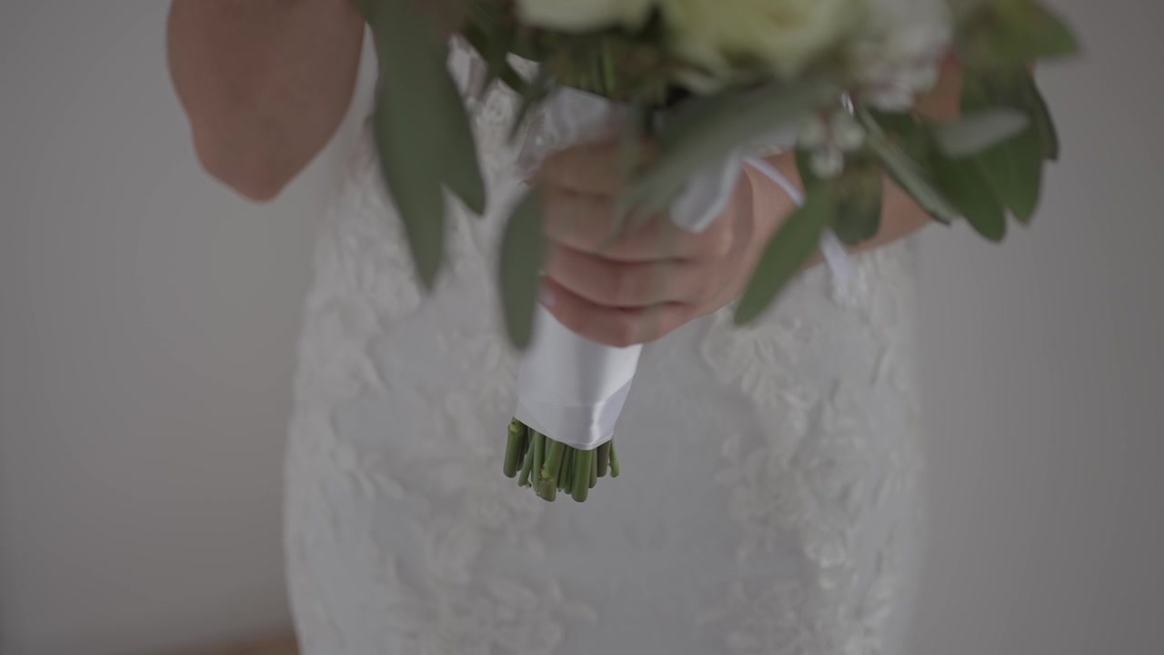 Vista aproximada das mãos da noiva segurando um buquê de flores na frente do vestido de noiva.