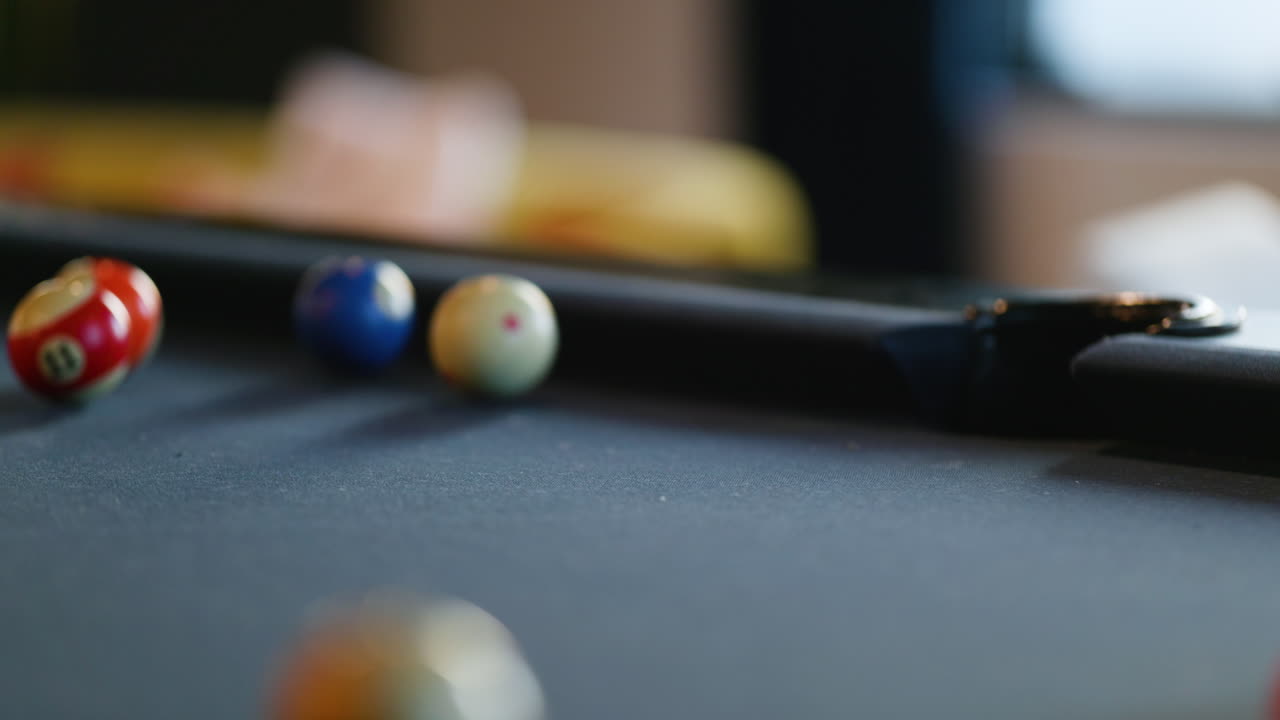 A group of colorful pool balls rolls across a dark felt table as players enjoy a friendly game in a cozy recreation center. The warm afternoon light adds to the inviting atmosphere.