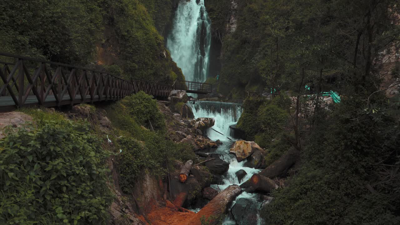vista de inclinación lenta hacia arriba de la cascada de peguche con puente de pasarela de madera en otavalo, ecuador