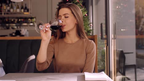 mujer disfrutando de un vaso de vino tinto en un restaurante durante la temporada de navidad