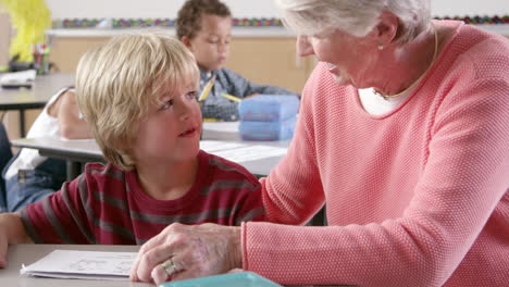 senior female teacher helping young schoolboy in class