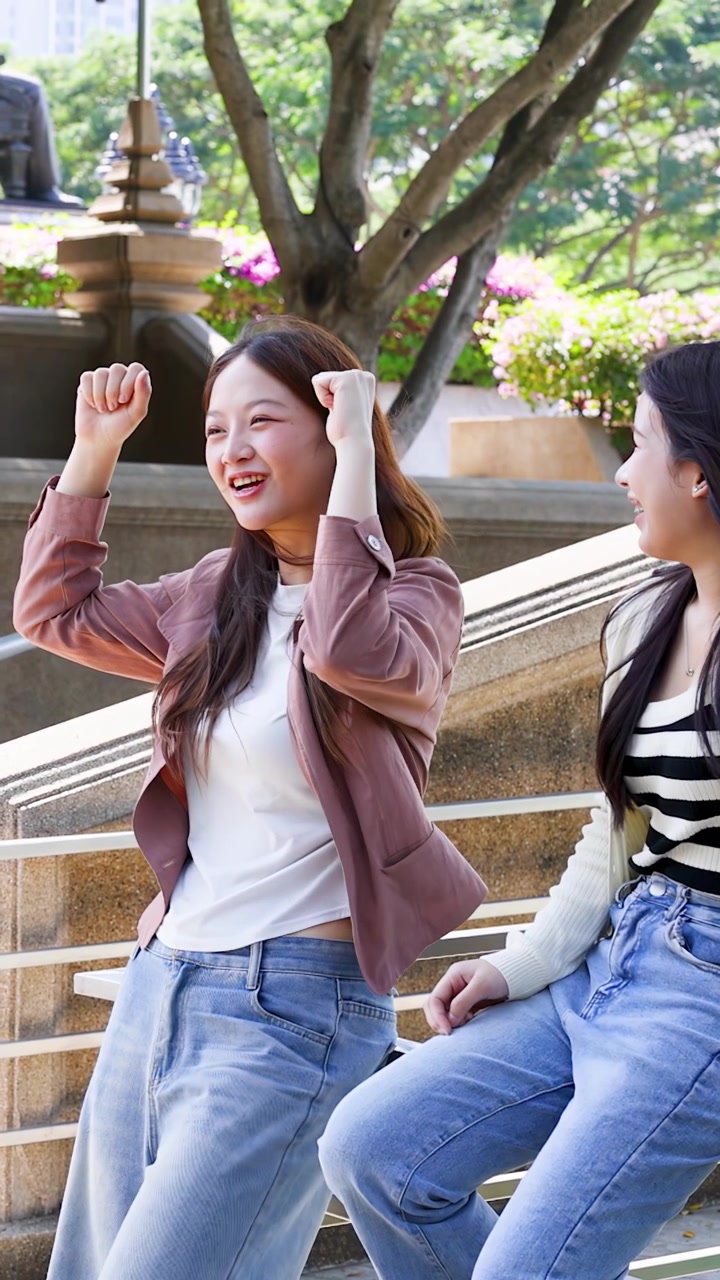 นักศึกษาไทยวัยหนุ่มสาวในชุดลำลองส่งเสียงเชียร์และหัวเราะด้วยกันบนบันไดในมหาวิทยาลัยที่แดดจ้า
