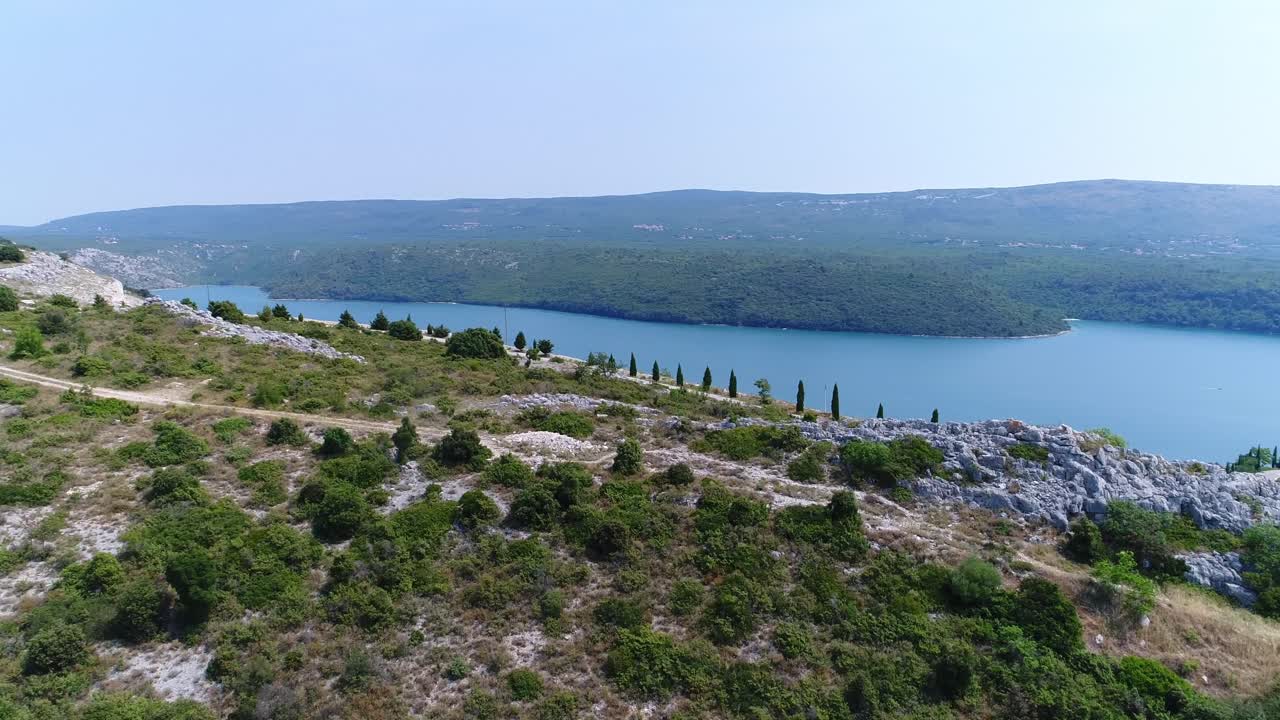 drone aéreo sobre la carretera de la colina del bosque de rakalj pula mar croacia, paisaje marino azul de islas verdes en la tranquila bahía croata de aguas turquesas
