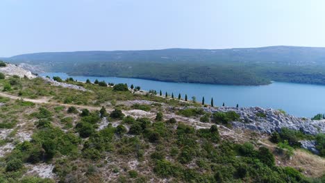 Drone-Aéreo-Sobre-La-Carretera-De-La-Colina-Del-Bosque-De-Rakalj-Pula-Mar-Croacia,-Paisaje-Marino-Azul-De-Islas-Verdes-En-La-Tranquila-Bahía-Croata-De-Aguas-Turquesas