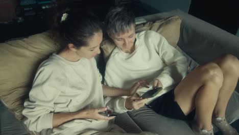 two women relaxing on a couch and using smartphones