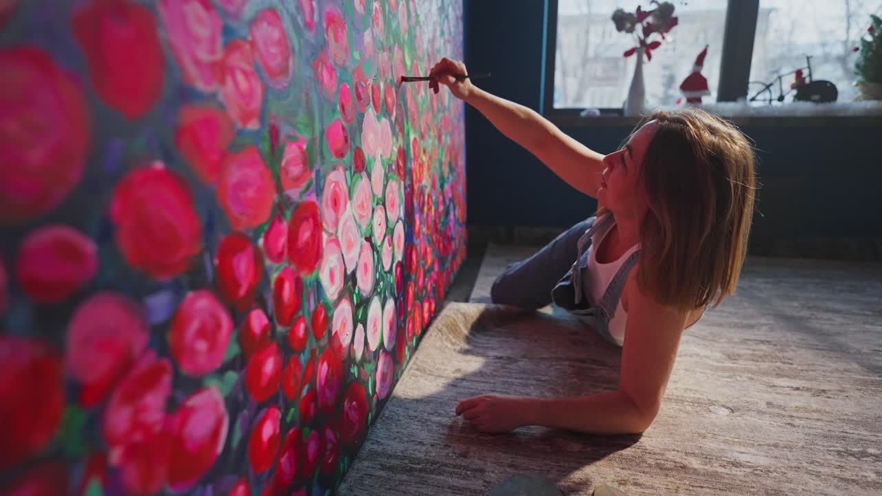 Kvindelig kunstner maler levende blomsterkunst på et stort lærred.