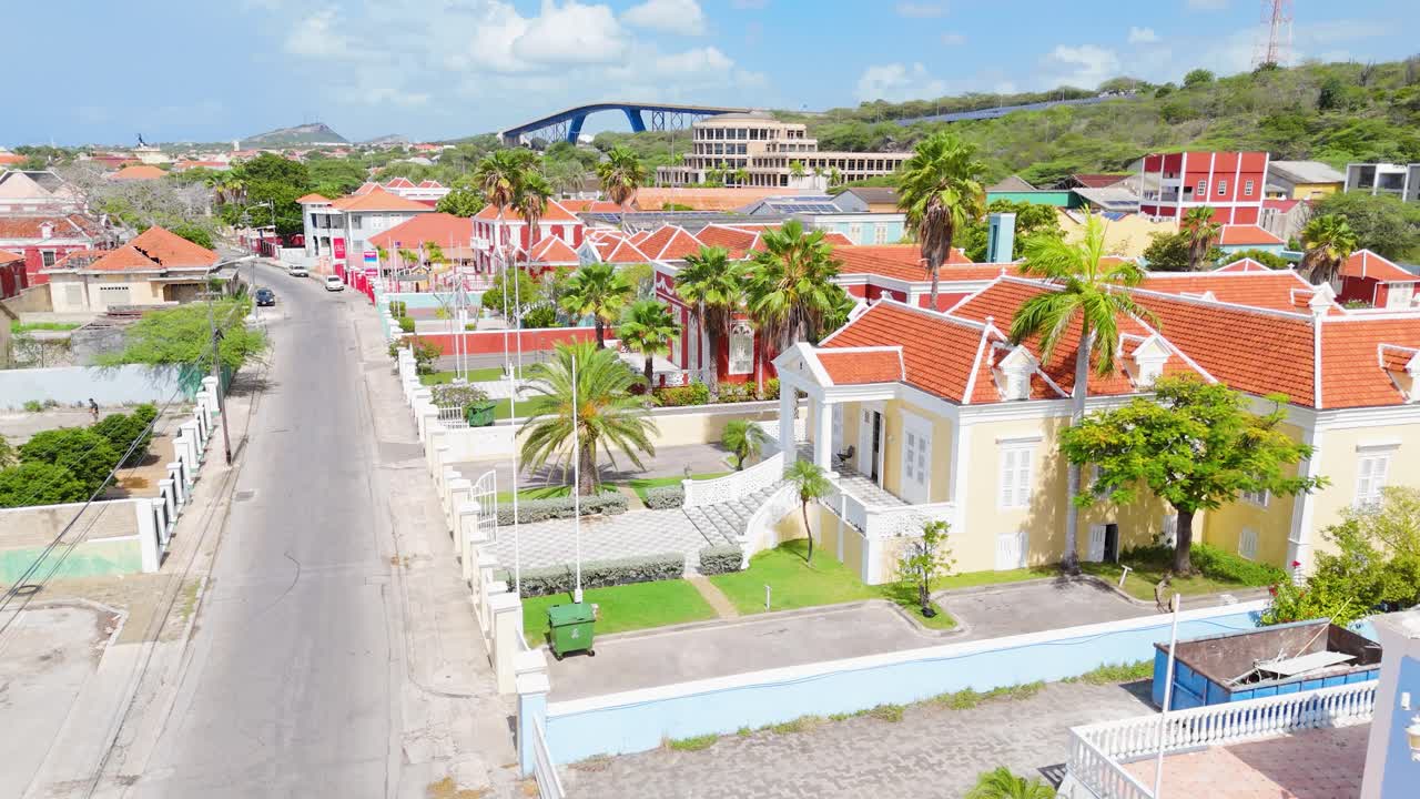 Drone descends to street level above fence in Scharloo District in Curaçao, showing vibrant rooftops and historic Caribbean architecture