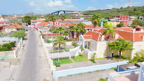 drone descends to street level above fence in scharloo district in curaçao, showing vibrant rooftops and historic caribbean architecture