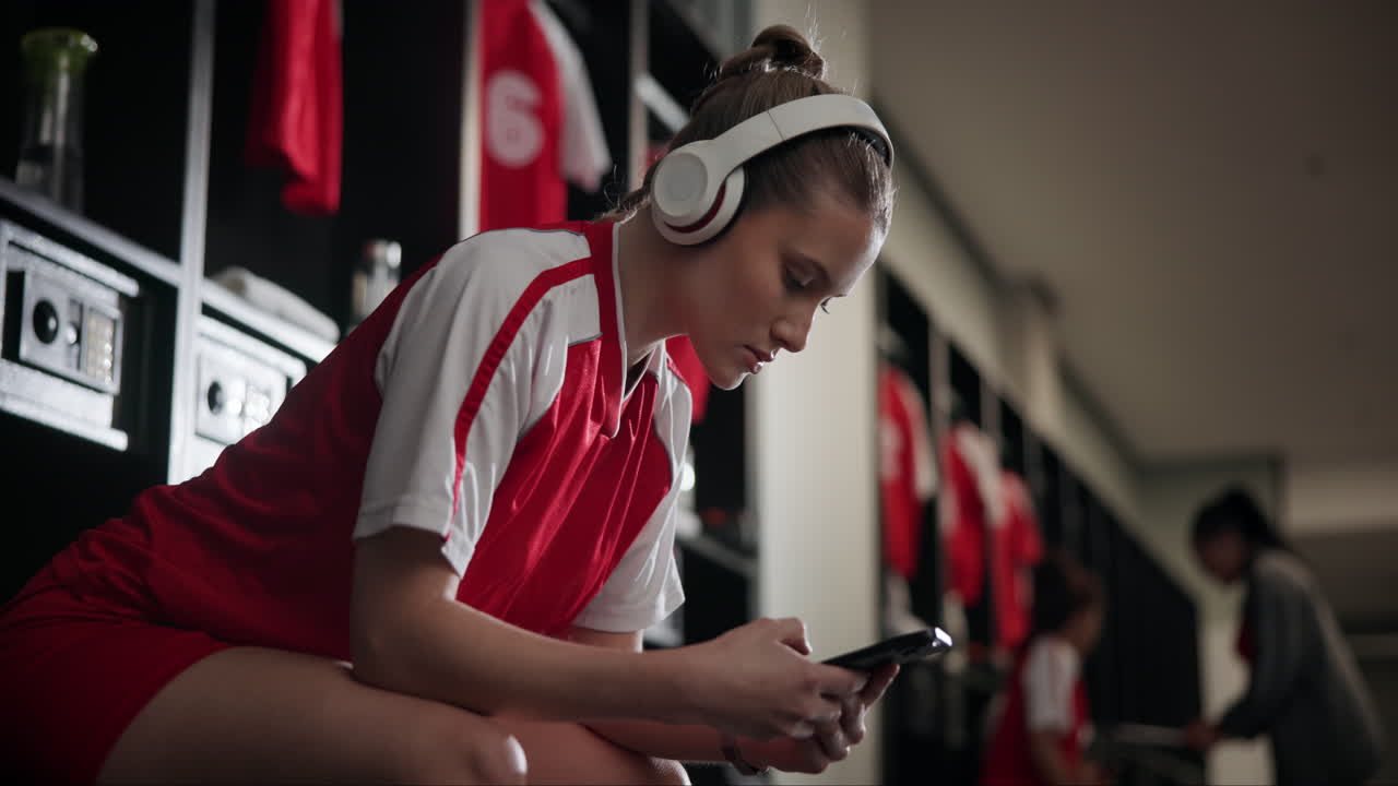 Woman in soccer uniform with headphones in a locker room