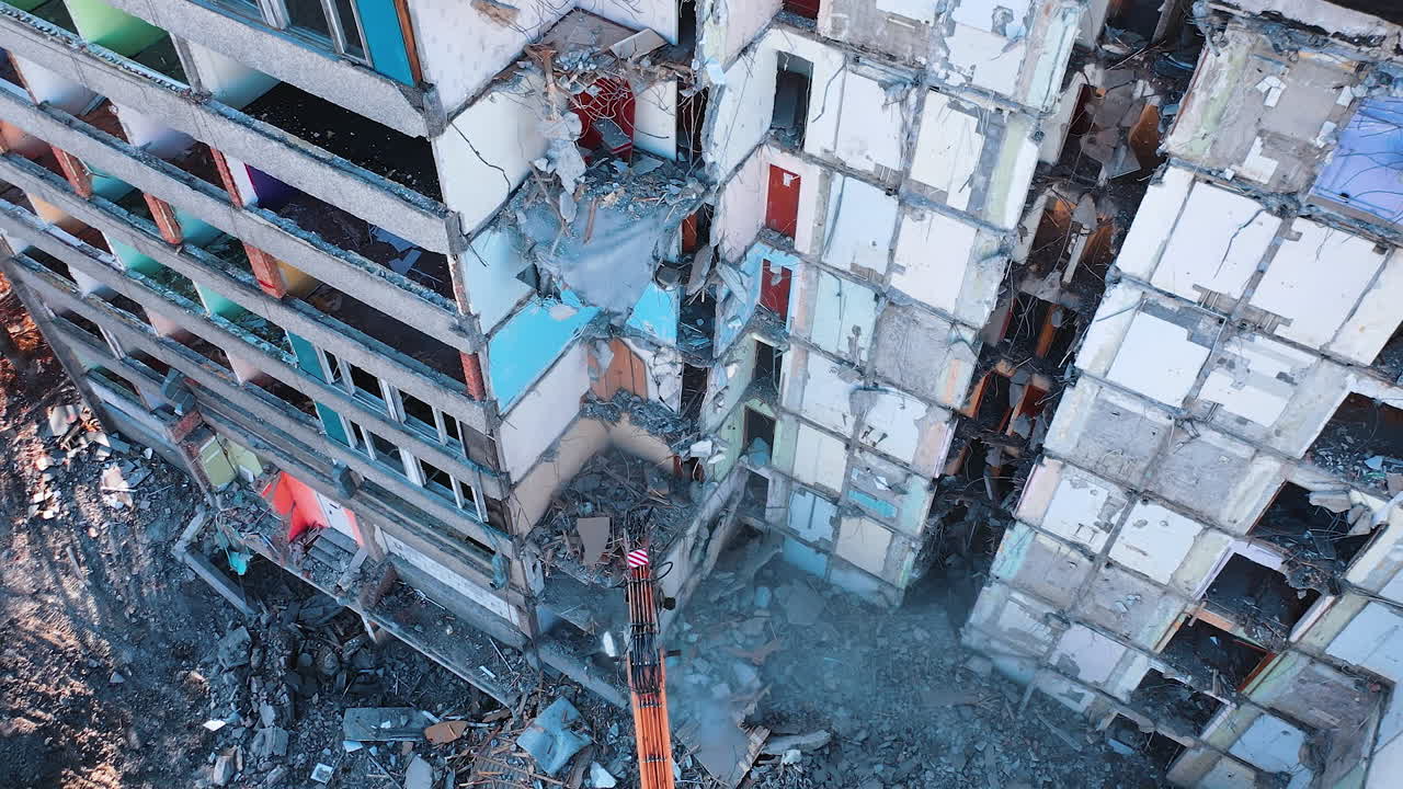 Deconstruction of old premises with the excavator claw. Heavy machinery demolishing debris and turning it into dust. View from above.