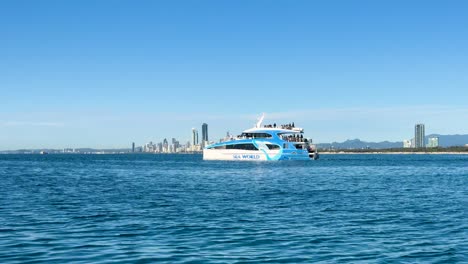 a tour boat moves steadily across calm blue water with the gold coast city skyline in the background under bright, clear daylight. wide, stable shot
