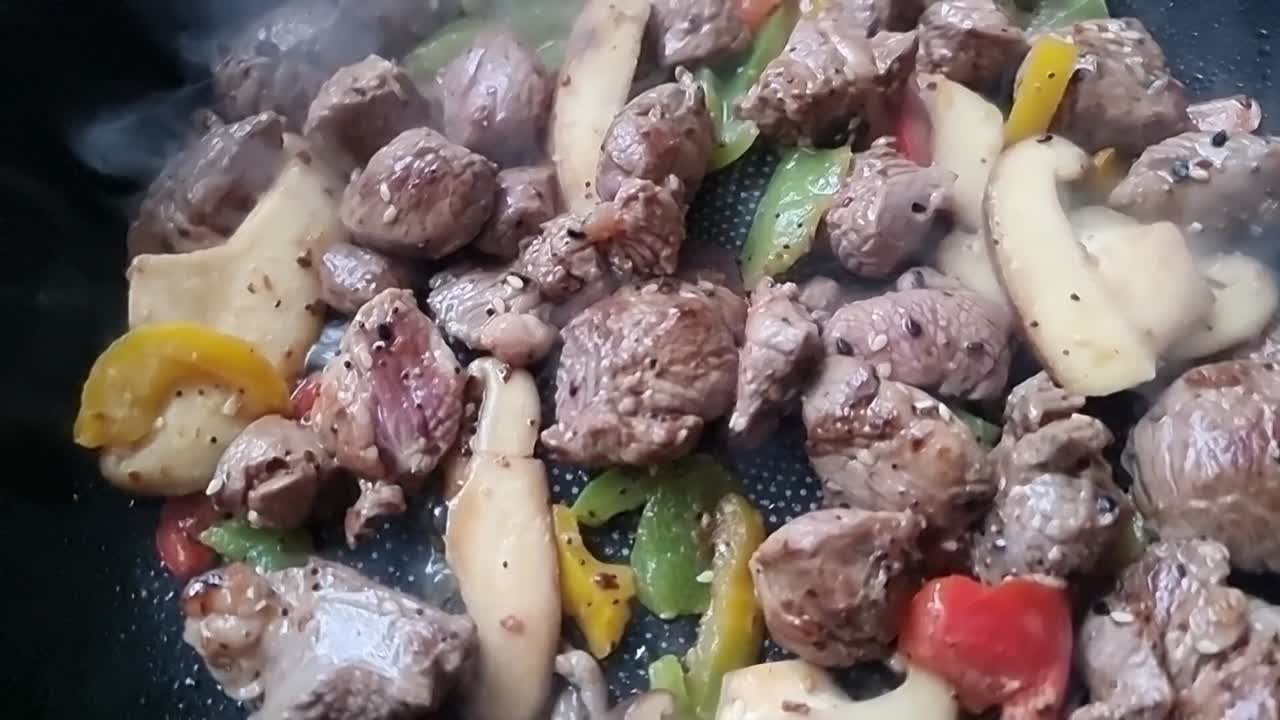 Daging domba potong dadu yang lezat dan mengepul dengan sayuran mendesis di wajan di atas kompor panas, diambil dari atas secara berputar.