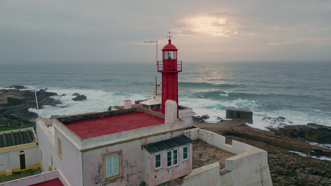 Aerial view beacon tower placed on gloomy seashore. Sunlight breaking clouds