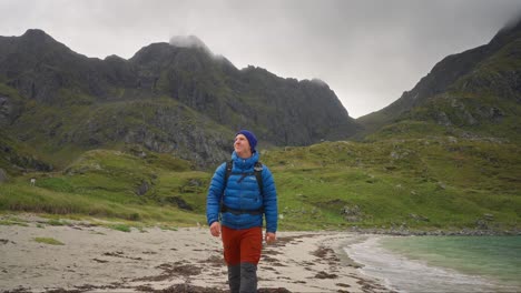 En-Cámara-Lenta,-Un-Joven-Con-Una-Chaqueta-Aislante-Azul-Camina-Sonriendo-En-Una-Playa-En-Las-Islas-Lofoten,-Noruega