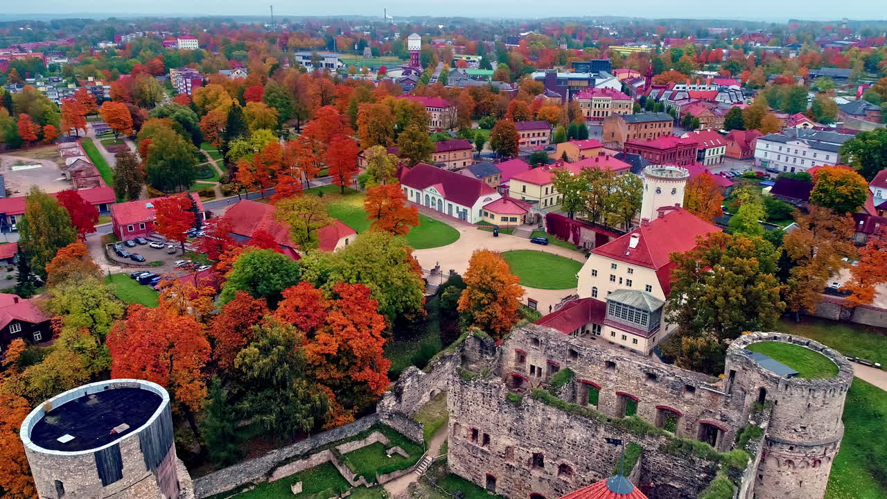 vista aérea de un castillo medieval icónico llamado castillo cēsis en letonia rodeado de árboles otoñales durante el día