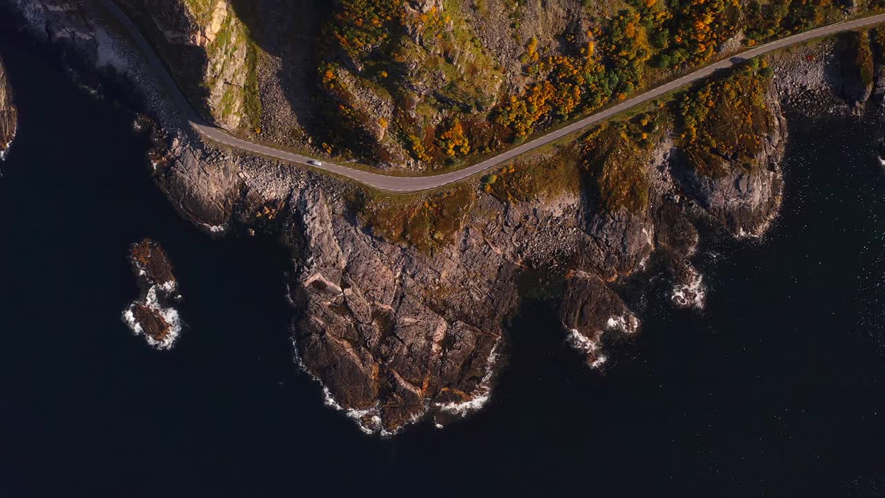 Winding road along a rocky coastline with waves crashing on the shore in Vestarelen