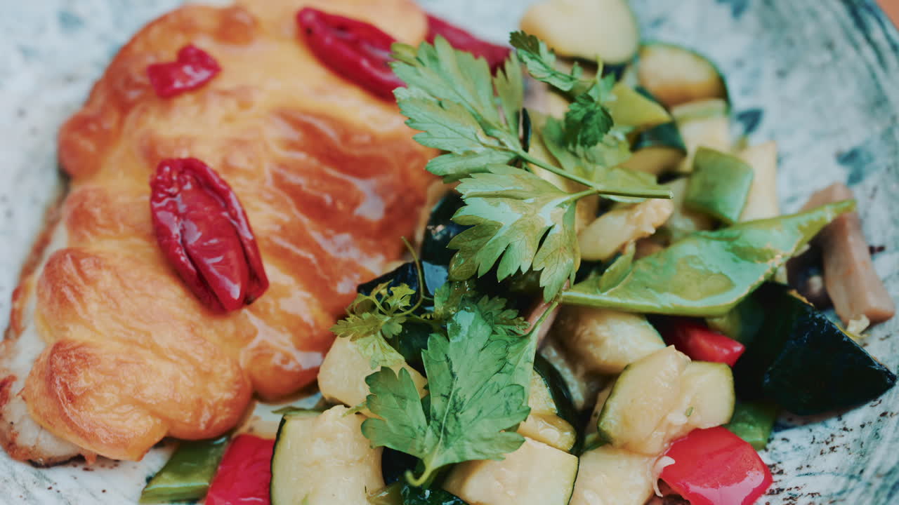 Close up of a golden croissant served with sauteed vegetables and fresh herbs
