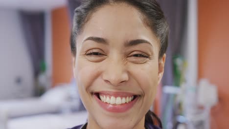 retrato de una feliz doctora biracial sonriendo y mirando a la cámara en el hospital