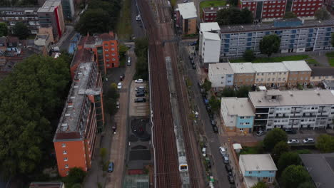 Forwards-tracking-of-train-driving-on-multi-track-railway-line-through-neighbourhood.-Aerial-view-of-transport-vehicle.-London,-UK