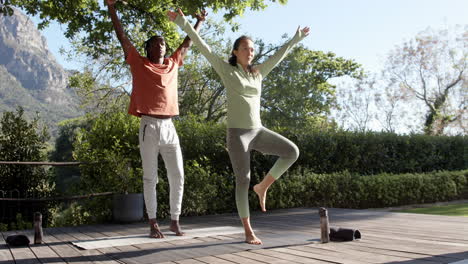 Happy-diverse-couple-practicing-yoga-standing-in-sunny-garden,-copy-space,-slow-motion