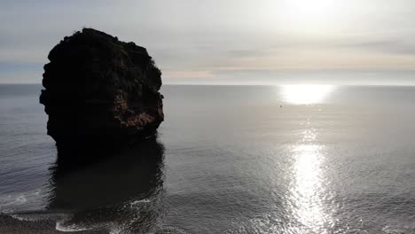 aerial silhouette view of lone sandstone sea stack alone surrounded by calm sea waves off ladram bay