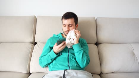 Hombre-Aburrido-Usando-El-Teléfono-En-El-Sofá-Mientras-Se-Aplica-Hielo-En-La-Cara