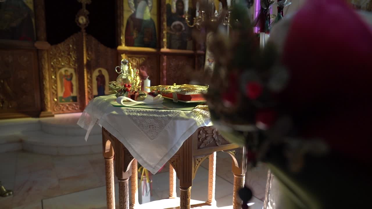 A Bible rests on a wooden table as the camera slowly moves back, revealing a decorated baptismal font entering the frame. Warm, ceremonial, and cinematic