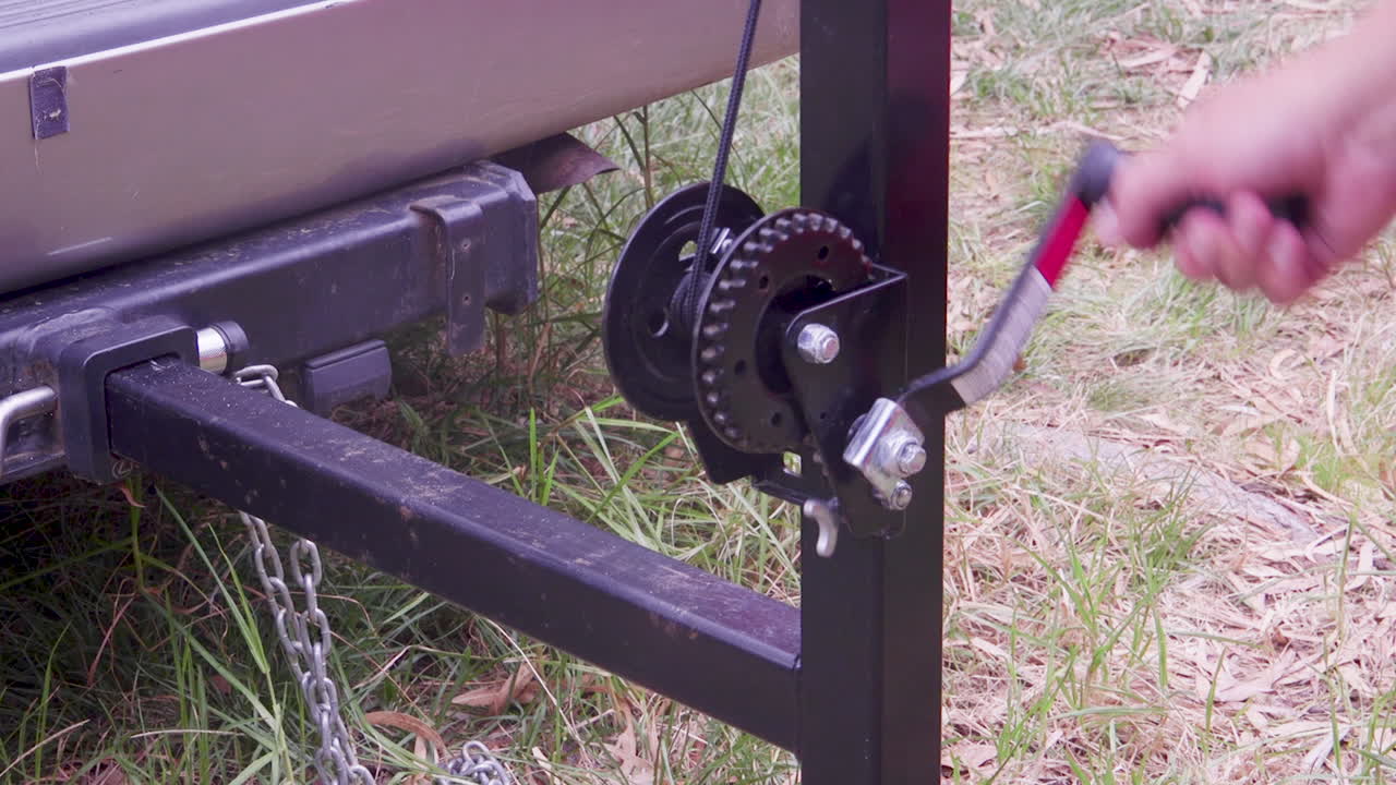 A person is manually winding a winch, demonstrating the operation of outdoor equipment in a natural setting. The scene captures the practical use of tools for various applications.