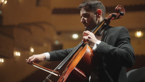 handsome cellist is playing classic music on scene of opera house concert or rehearsal